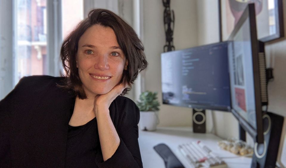 Me, in front of my desk, not directly looking into the camera. I'm smiling and wear a blazer I wouldn't normally wear when I'm working